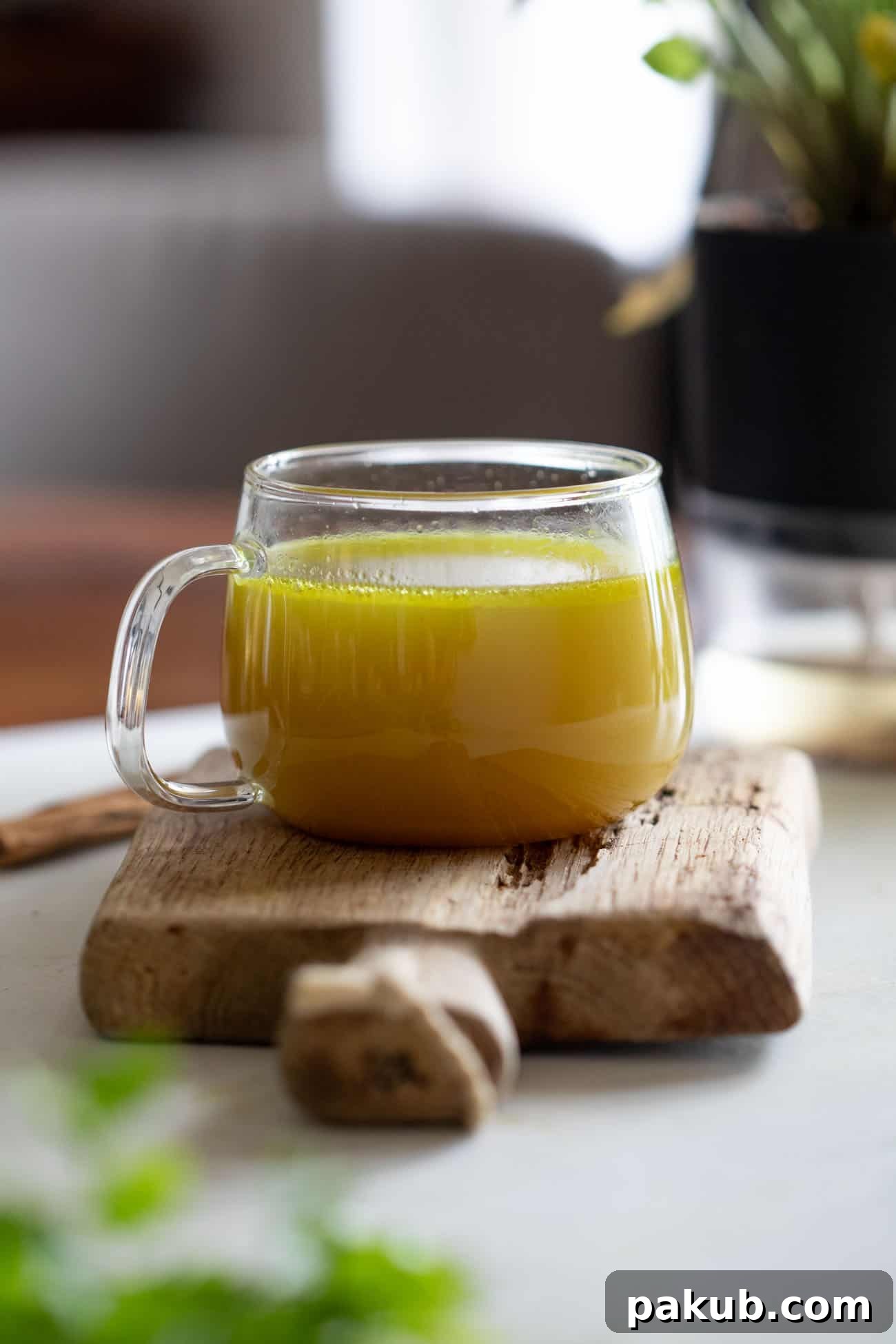 Liquid Gold Chicken Broth 5 A cozy shot of a clear glass mug filled with golden turmeric chicken broth, resting invitingly on a wooden board, ready to be enjoyed.
