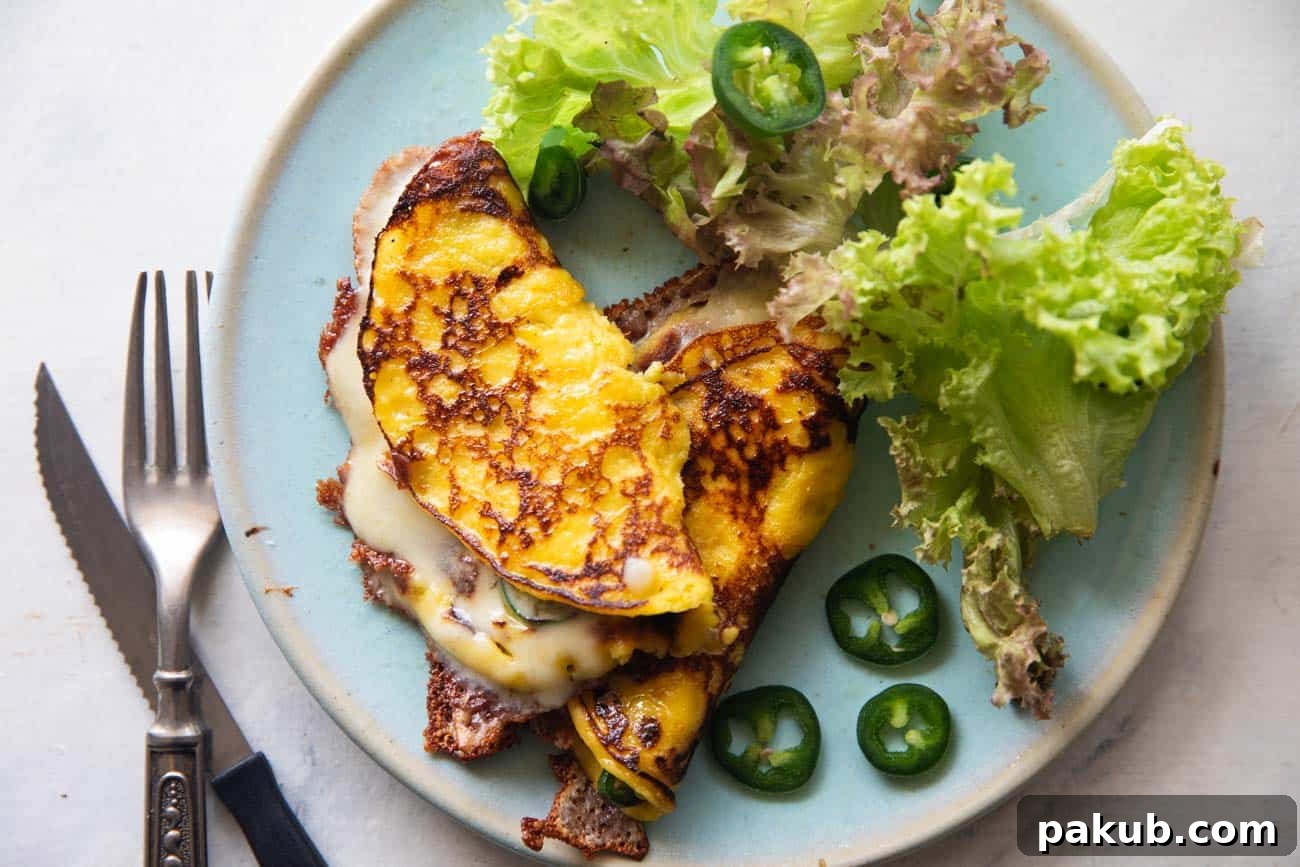 Venezuelan Cachapas Golden Corn Pancakes 6 A vibrant image of a folded cachapa, filled with melted cheese, on a blue plate. It's accompanied by fresh green lettuce and sliced jalapeños, suggesting a perfect balance of flavors and textures.