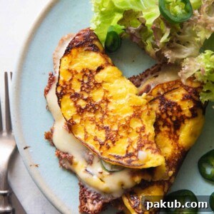 An image of cheese filled cachapa on a blue plate with sliced jalapeno and lettuce on the side
