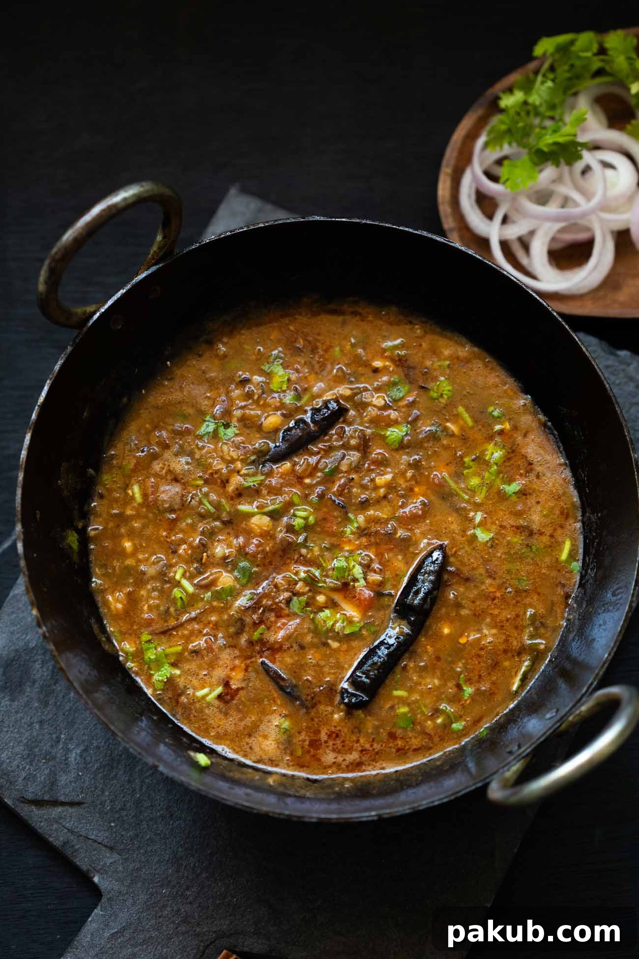 Hearty Dhaba Dal Blend 6 A beautiful black kadhai filled with Dhaba style Mixed Dal, accompanied by a small bowl of fresh sliced onions, ready to be served.