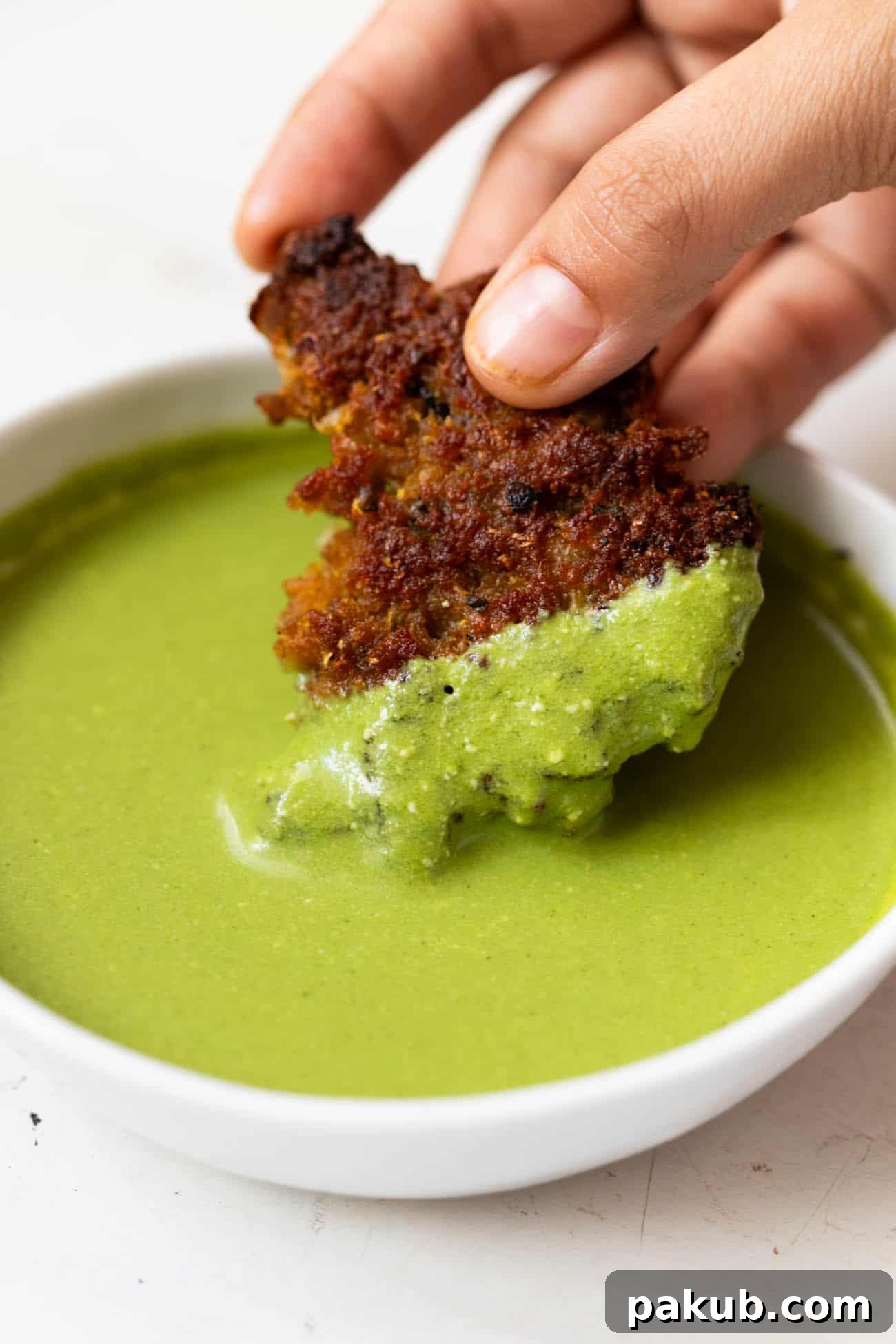 A delicious chapli kebab being dipped into a bowl of fresh mint chutney, highlighting its perfect pairing.