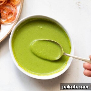 Mint chutney served in a white bowl with a spoonful being taken out, showcasing its rich texture.