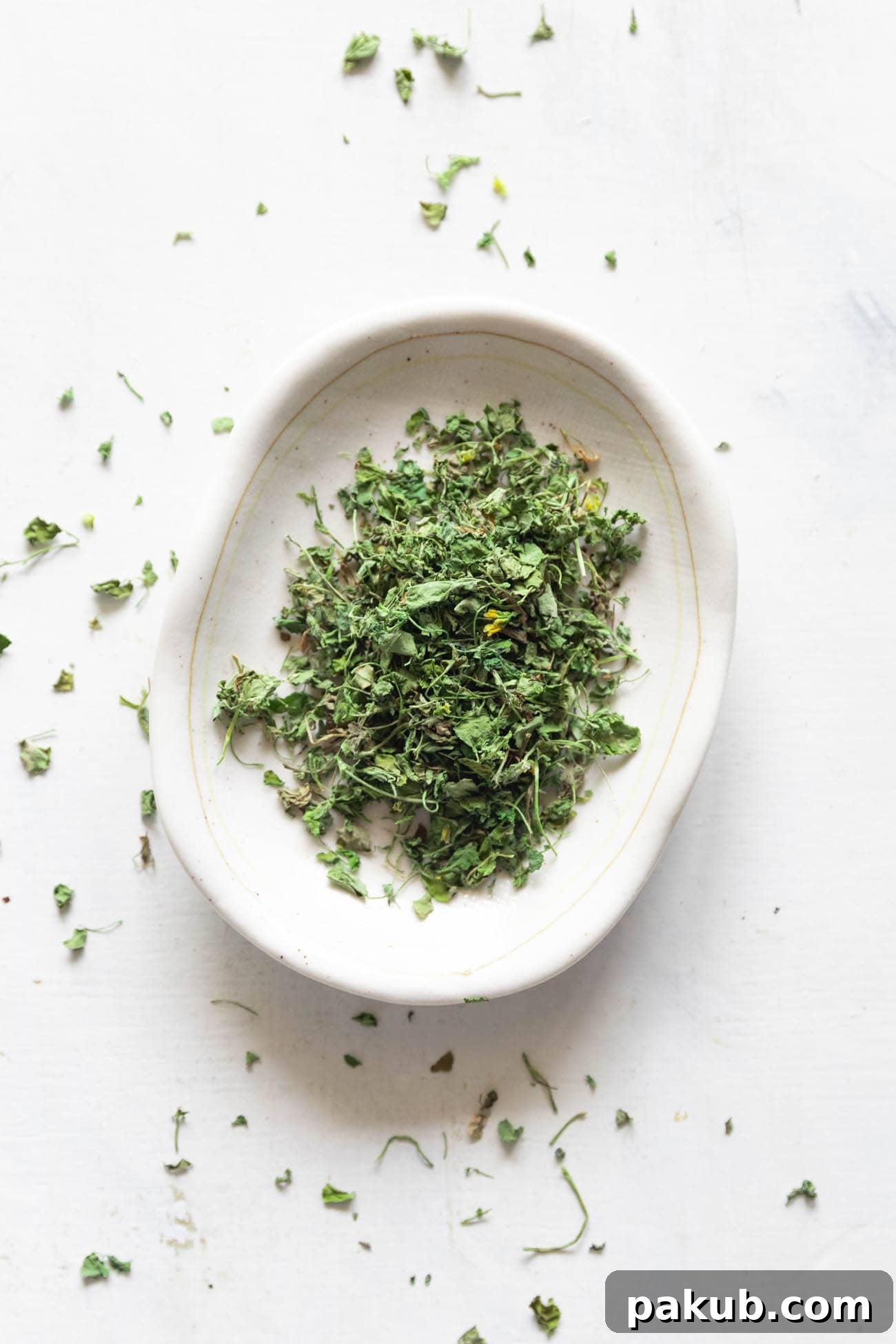Kasuri Methi Your Complete Guide to Dried Fenugreek Leaves and Their Uses 2 Close-up shot of dried Kasuri Methi leaves on a pristine white plate, showcasing their delicate texture and verdant hue, ready to be incorporated into an Indian dish.