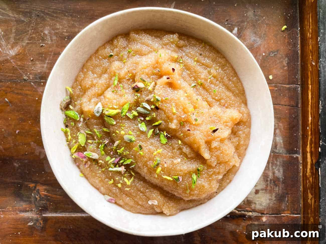 Irresistible Sooji Halwa 5 A beautifully presented white bowl of Sooji Halwa, generously sprinkled with bright green pistachios on top, highlighting its rich texture and appealing color.