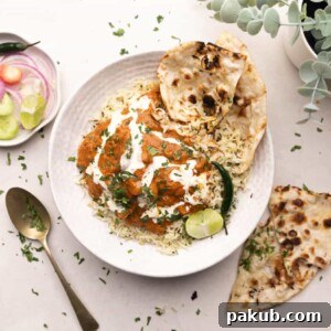 A comforting plate of slow cooker chicken tikka masala, generously drizzled with cream and served atop fluffy rice with a side of naan.