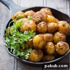 Bombay potatoes garnished with fresh coriander and served invitingly in a rustic black pan, ready to be devoured as a zesty appetizer.
