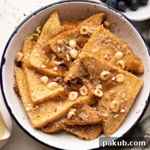 A warm, inviting cinnamon bread pudding, lightly brushed with butter and served in a round enamel baking dish, accompanied by fresh blueberries and a rich rum custard sauce.