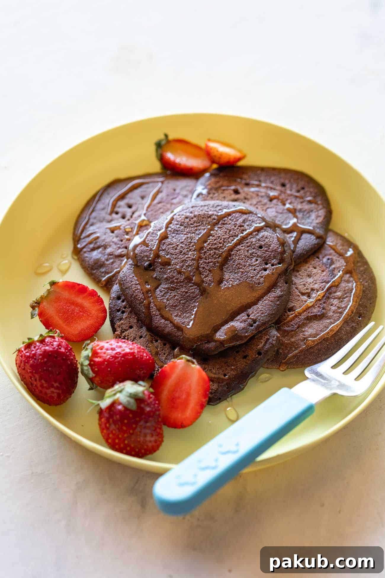 Delicious Chocolate Ragi Pancakes served on a vibrant yellow plate, gracefully drizzled with golden honey and accompanied by fresh, juicy strawberries, ready to be enjoyed.