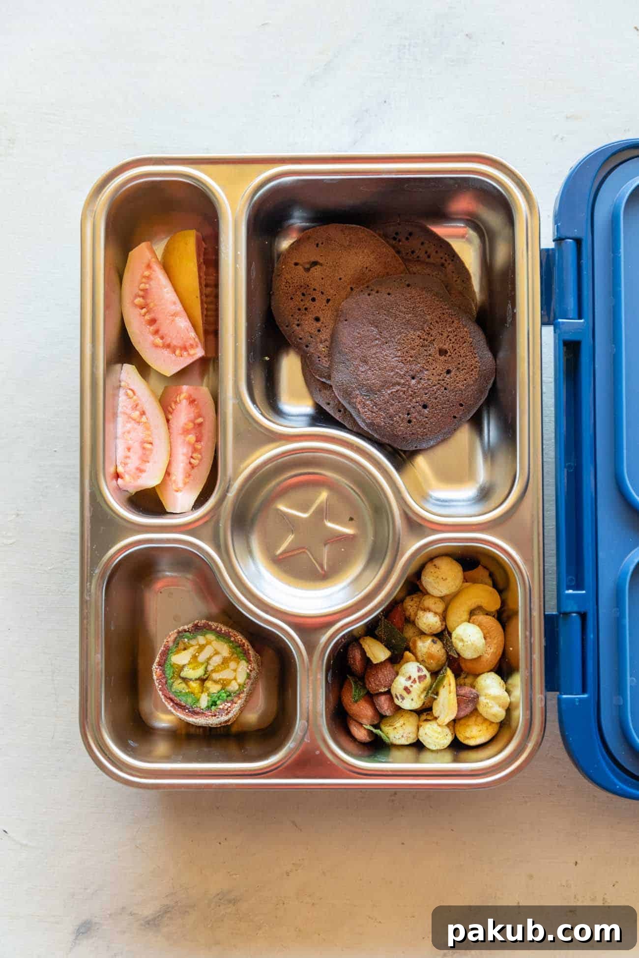 A vibrant and balanced lunch box filled with healthy Chocolate Ragi Pancakes, fresh guava, crunchy roasted makhanas, and a small traditional sweet (mithai), perfect for a child's tiffin.