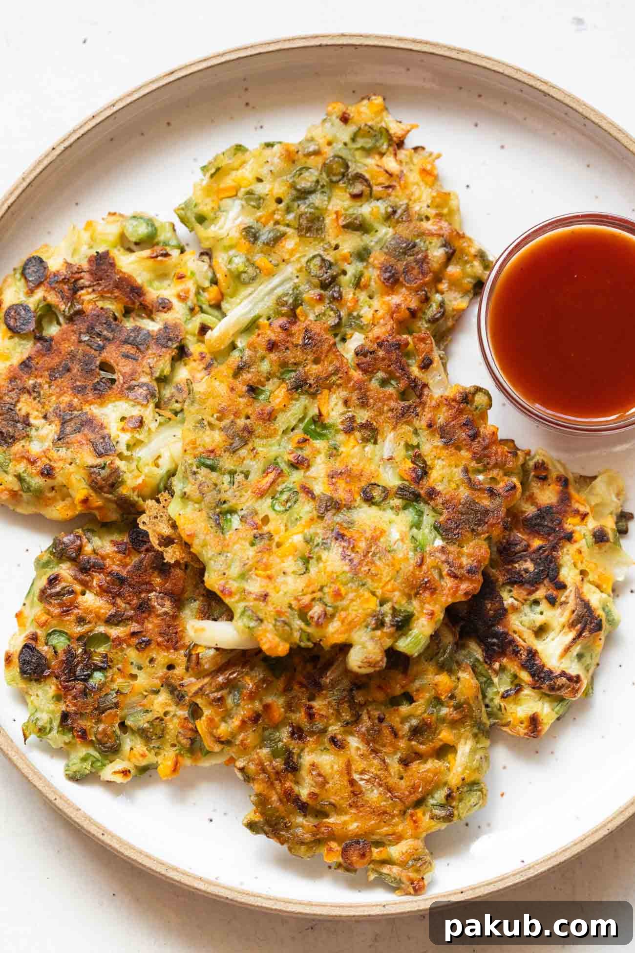Crispy golden-brown vegetable pancakes served on a white plate with a side of bright red ketchup, ready for dipping.