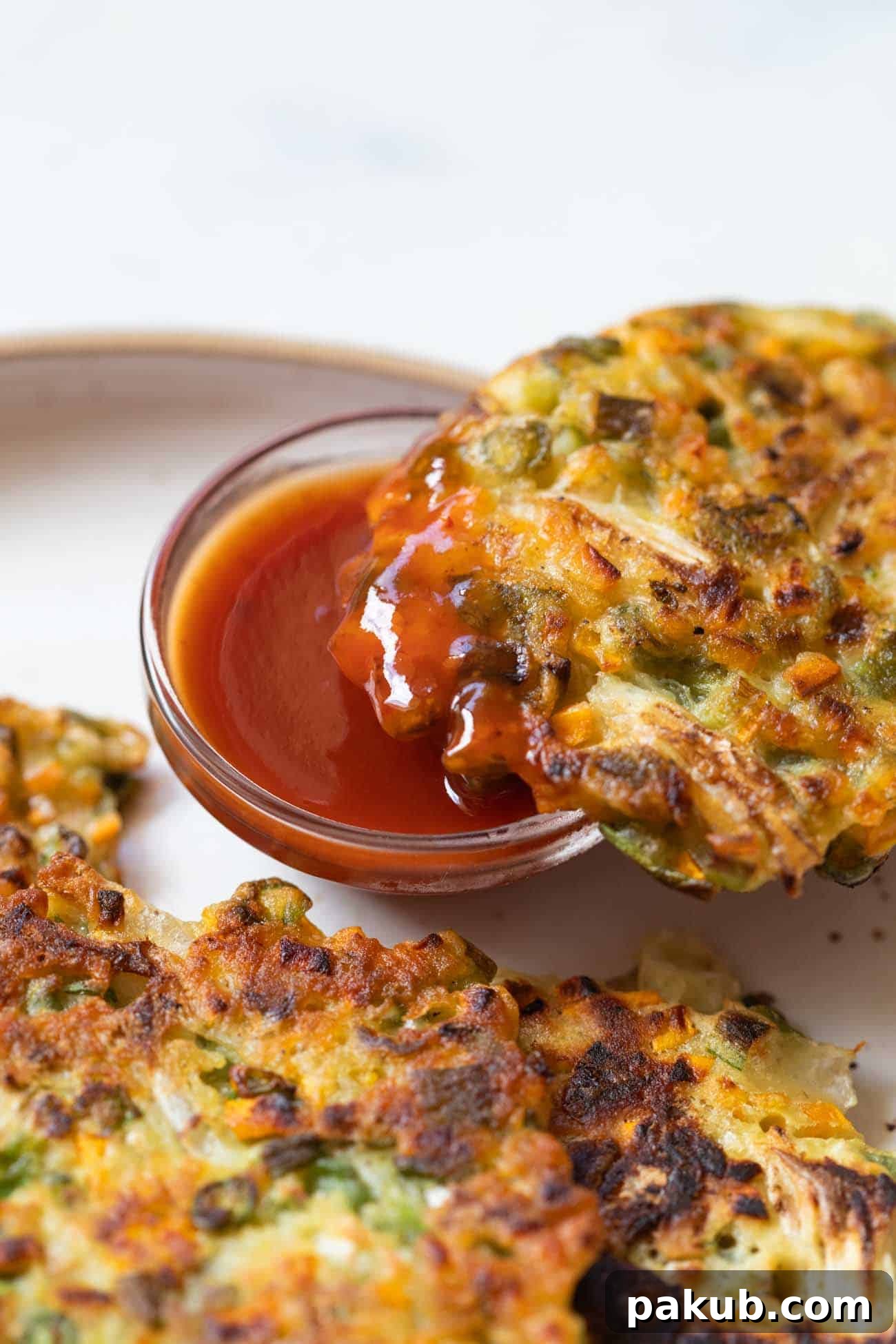 A beautifully stacked serving of golden-brown, crispy vegetable pancakes, garnished with fresh green onions, showcasing their appealing texture and vibrant colors, ready to be enjoyed with a dip.