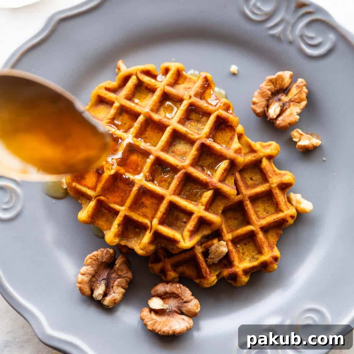 Golden Pumpkin Spice Waffles 2 Spoon drizzling honey over two pumpkin waffles served on a plate, highlighting their golden brown and fluffy texture.