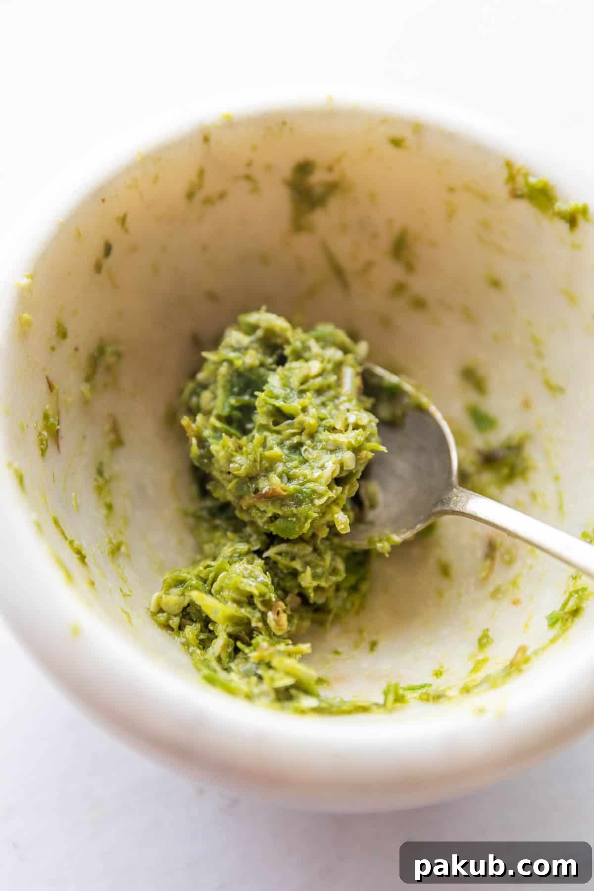 Spicy Naan Fusion: Chilli Garlic and Thecha 3 A close-up shot of green chilli and garlic thecha in a white mortar and pestle bowl, with a spoon