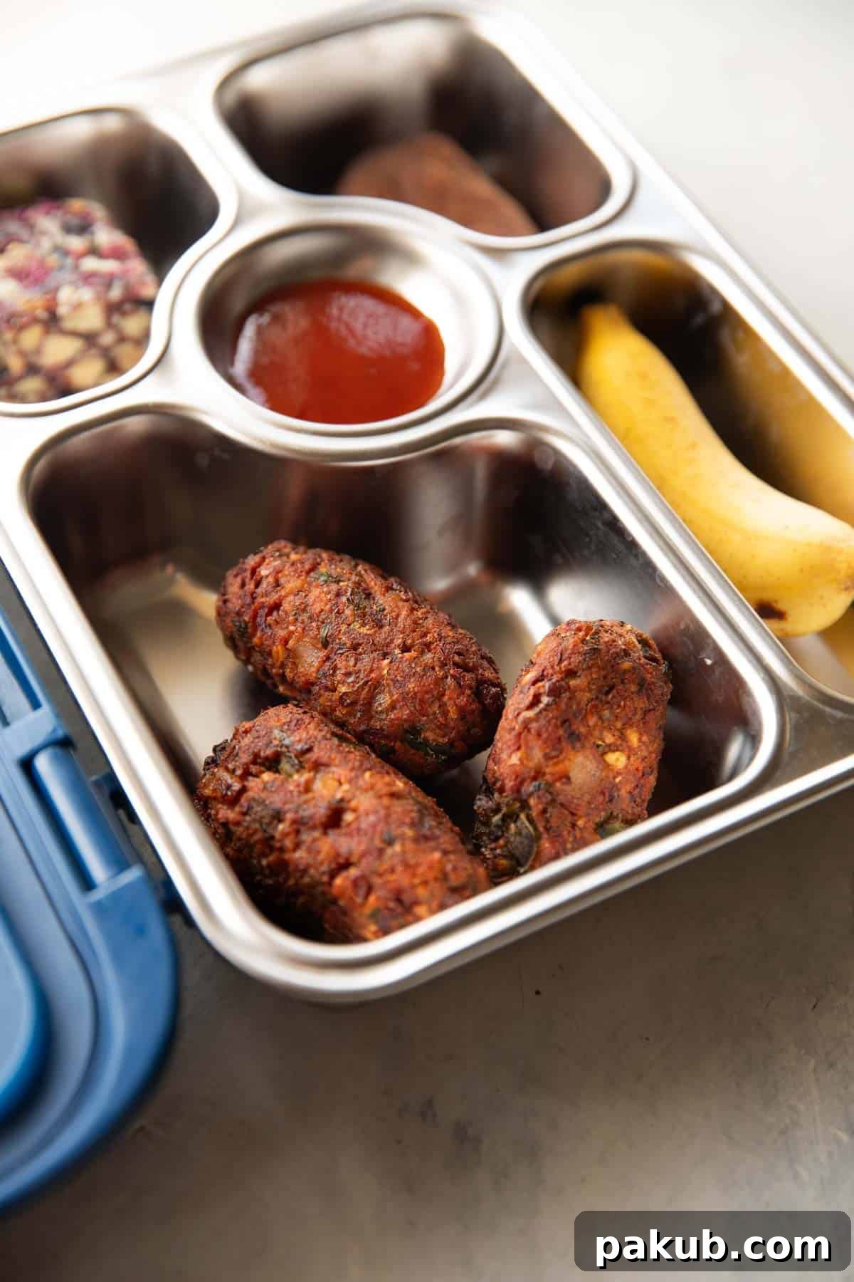 A vibrant lunch box featuring crispy sprouts cutlets, a sweet treat, fresh banana, and a small container of ketchup, highlighting a healthy and appealing meal.