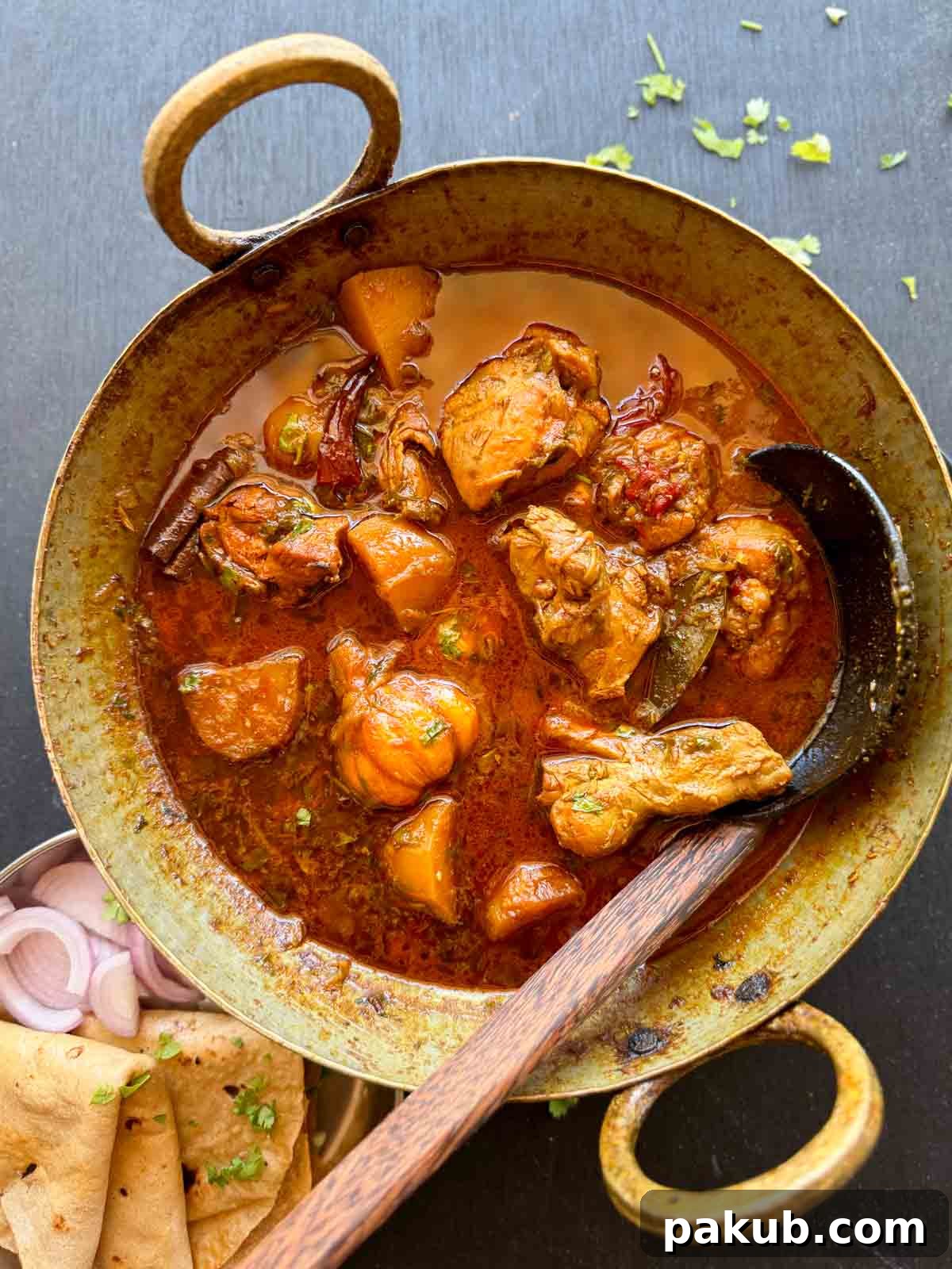 Authentic Bihari Chicken Curry served in a traditional Indian kadhai, garnished with fresh cilantro, accompanied by warm rotis and sliced red onions.