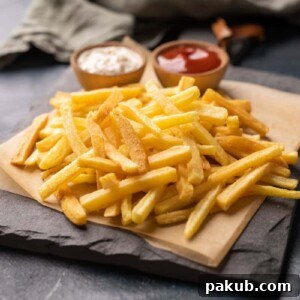 A plate of perfectly golden homemade French fries, accompanied by a creamy mayonnaise dip and a generous dollop of ketchup.