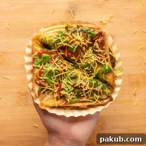 A hand holding a perfectly grilled Bombay Sandwich Toast on a paper plate, ready to be devoured.