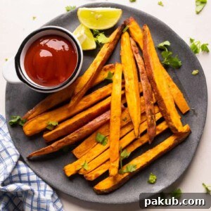 Baked sweet potato fries served on a sleek grey plate, accompanied by ketchup and fresh lime wedges.
