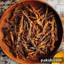 Golden-brown baked kurkuri bhindi, a crispy okra dish, served in an earthy brown bowl.