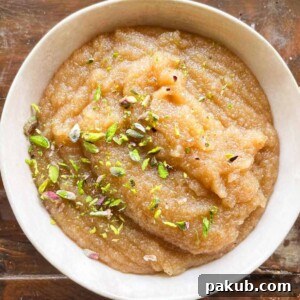 A beautiful white bowl filled with warm Sooji Halwa, generously sprinkled with chopped pistachios.