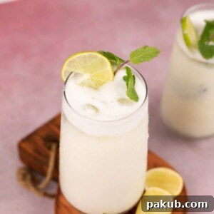 A glass of creamy Limonada, also known as Brazilian Lemonade, garnished with a sprig of fresh mint and slices of lemon.
