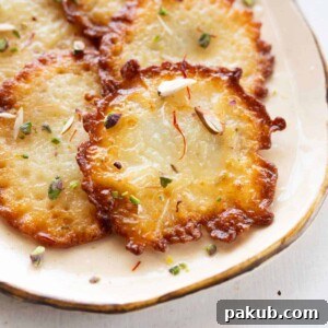 A close up shot of malpua arranged on a white plate with nuts and saffron sprinkled on top