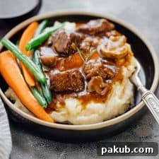 Hearty Pressure Cooker Beef Bourguignon, served with creamy mashed potatoes and grilled vegetables on a black plate.
