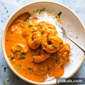 Rich Goan prawn curry with coconut, generously ladled over fluffy steamed rice and served in a white bowl with a fork.