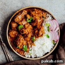 Rich slow cooker lamb curry served on a plate with fluffy rice and fresh sliced onions.