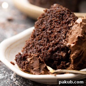 A luscious slice of chocolate cake, generously topped with rich chocolate buttercream, with a spoon taking a bite.