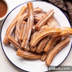 Perfectly fried churros piled high on a plate, served with a rich chocolate dipping sauce.