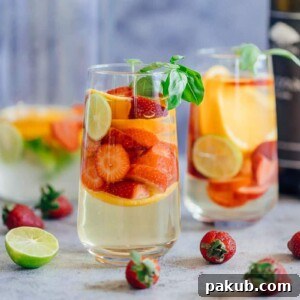 Vibrant Strawberry Orange White Wine Sangria, served in two elegant glasses with fresh limes and basil leaves.