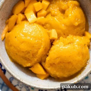Mango sorbet scoops served in a brown ceramic bowl with diced mangoes, highlighting its smooth texture.