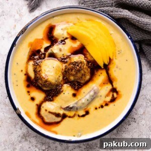 Mango Kadhi served in a blue and white enamel bowl with mango slices and tadka on top.