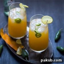 Tall Mango Jalapeno Fizzy Cocktail served with ice and a slice of lime in glasses resting on a brown tray.