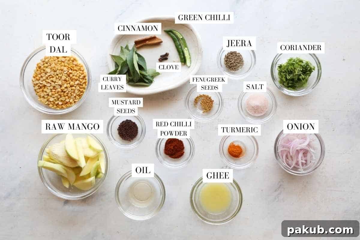 Zesty Raw Mango Lentil Curry 3 Assorted ingredients for raw mango dal, including toor dal, sliced raw mangoes, green chilies, spices, and tempering ingredients, neatly arranged in transparent bowls.