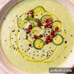 A bowl of refreshing Cold Cucumber Soup, beautifully garnished with crisp cucumber slices, jewel-like pomegranate seeds, and nigella seeds, ready to be served as a cooling starter.