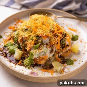 A delightful Bread Chaat served on a pristine white plate with a spoon, adorned with various chutneys and crispy sev, ready to be enjoyed.