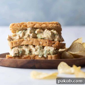 A delectable Curry Chicken Salad Sandwich, served alongside crispy potato chips on a plate, offering an Indian-inspired twist on a classic.