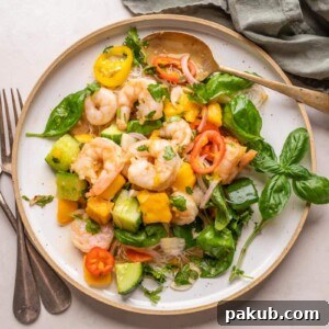 A colorful Thai Prawn Mango Salad elegantly served on a white plate with cutlery, showcasing plump prawns, fresh mango, and vibrant herbs.