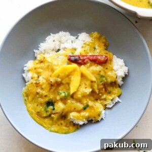 A comforting serving of Raw Mango Dal (Mamidikaya Pappu) presented with steamed rice in a grey bowl, offering a unique blend of spicy and sour flavors.