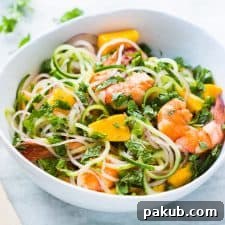 A refreshing Cucumber Noodle Prawn and Mango Salad, gluten-free and served in a crisp white bowl, featuring spiralized cucumber noodles and succulent prawns.