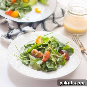 A wholesome Spinach, Heirloom Tomato, and Crumbled Tofu Salad, elegantly served in a white bowl, highlighted by a rich Roasted Garlic Dressing.