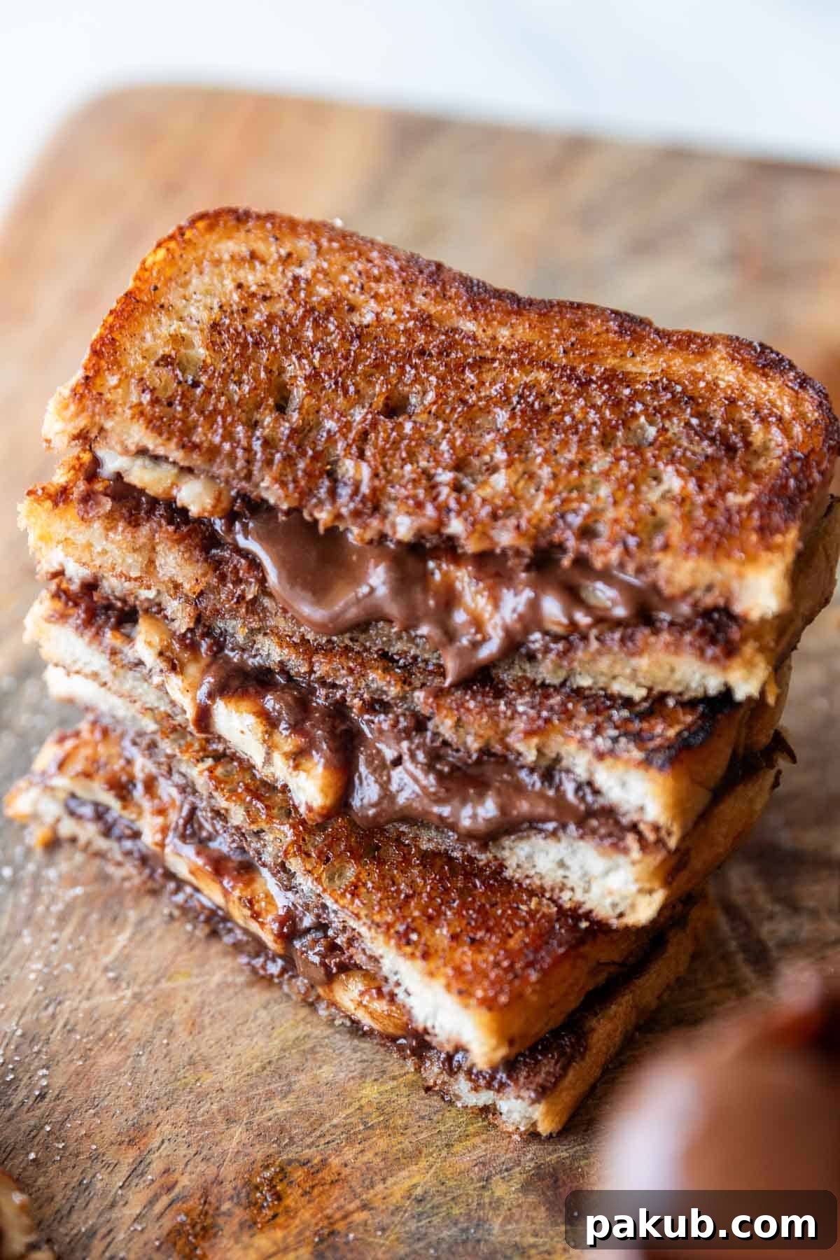 Grilled chocolate banana sandwich on a rustic wooden board, sliced in half with melted chocolate and banana slices visible.