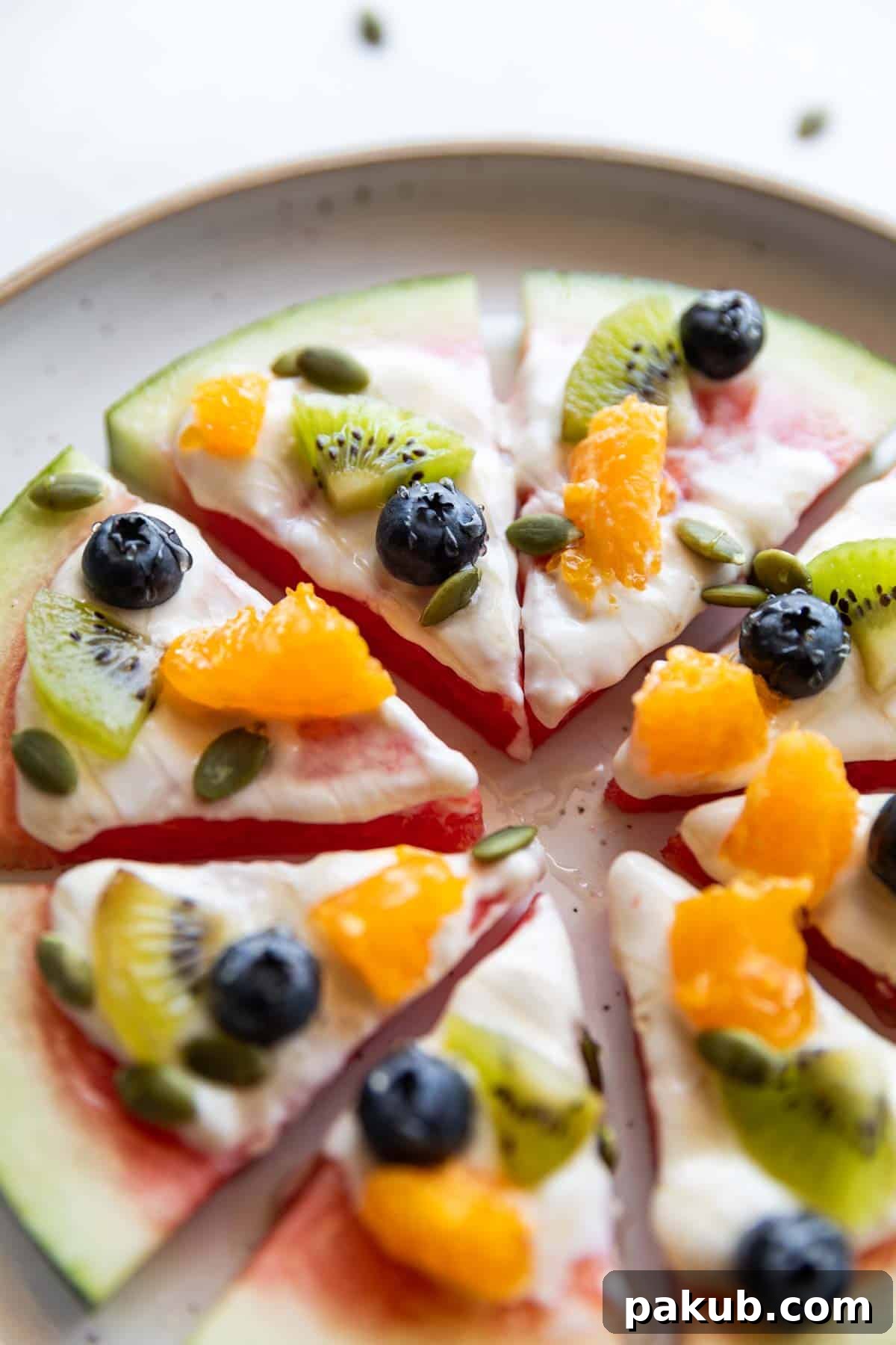 Watermelon Wonder Wheels 4 Close-up of vibrant watermelon pizza slices, elegantly arranged on a white serving plate, highlighting the fresh fruit toppings and creamy glaze