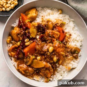 Delicious Kung Pao Chicken served generously over steamed rice in a bowl, garnished with peanuts.