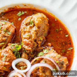 A bowl of pressure cooker chicken curry served with a side of sliced onion rings, garnished with fresh cilantro, ready to be enjoyed.