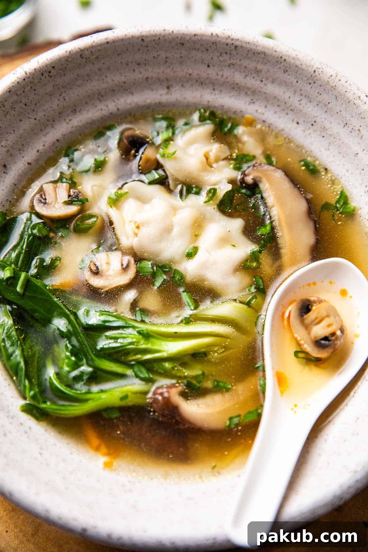 Steaming Wonton Perfection 3 Two white bowls of Wonton Soup on a wooden table, one with a spoon, highlighting the vibrant broth and plump wontons.