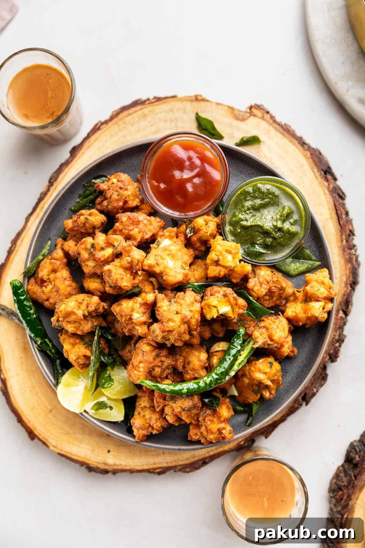 Spiced Egg Fritters 2 Crispy Egg Pakodas served with vibrant green chutney, tangy tomato ketchup, fried green chilies, and fresh lemon wedges, alongside a steaming cup of tea.
