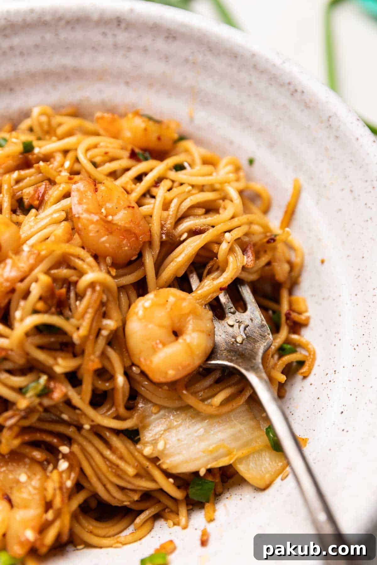 Spicy Garlic Prawn Noodle Stir-fry 3 A tantalizing close-up shot of chilli garlic prawn noodles in a white bowl, showcasing the glistening sauce, plump prawns, and thinly sliced spring onions.